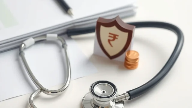 Stethoscope, shield symbol and coins on a desk representing health insurance cover